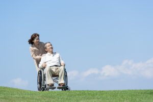 青空の下で車いすに座る男性と押す介護士の女性